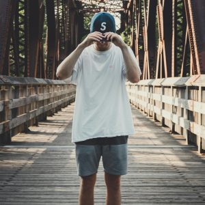 Casual fashion photo of a man posing on a metal bridge on a sunny day.